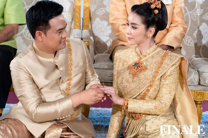 Mai Sukhonthawa exchanging rings in a gold long-sleeved Siwalai outfit with an embroidered shoulder drape.