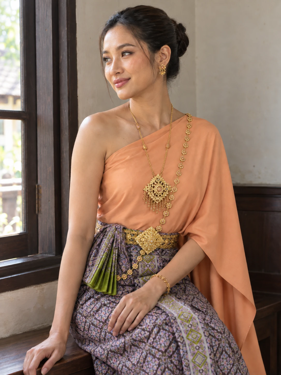 Chompoo in the peach Sabai and patterned skirt, seated beside a window